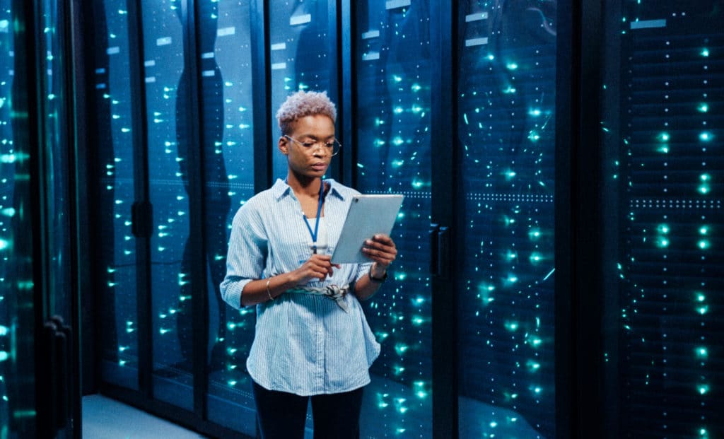 female excalibur IT administrator walking in server corridor diagnosing hardware system performance in data center cyber secure storage.